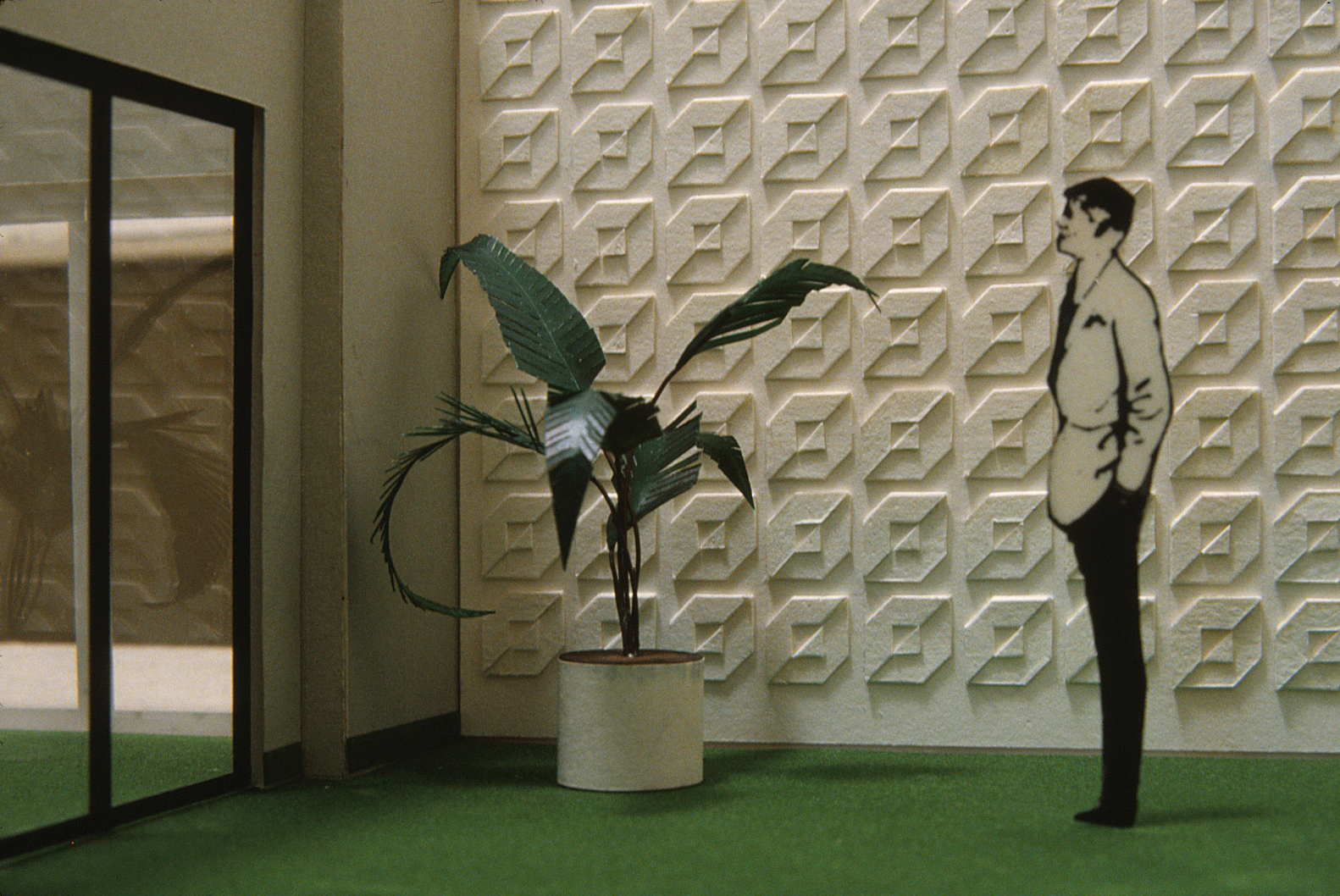 Model of an interior room in corporate headquarters featuring a repeat white on white logo on the wall, 
        with a plant, a door, and a man standing beside it.