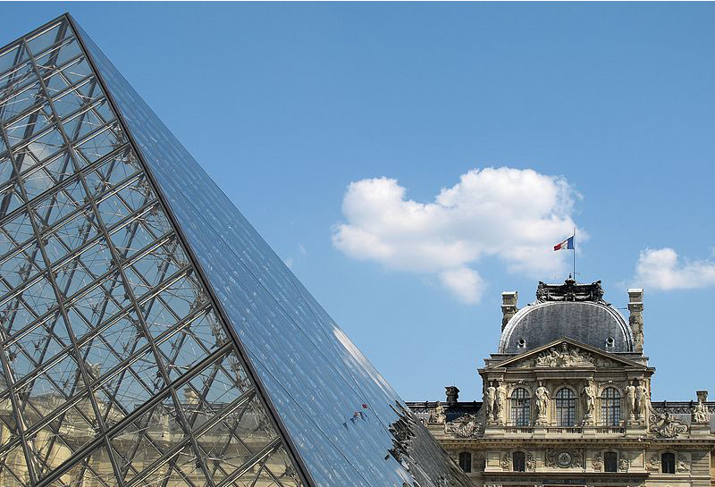 Closeup of the glass pyramid with the Louvre in the background behind it.