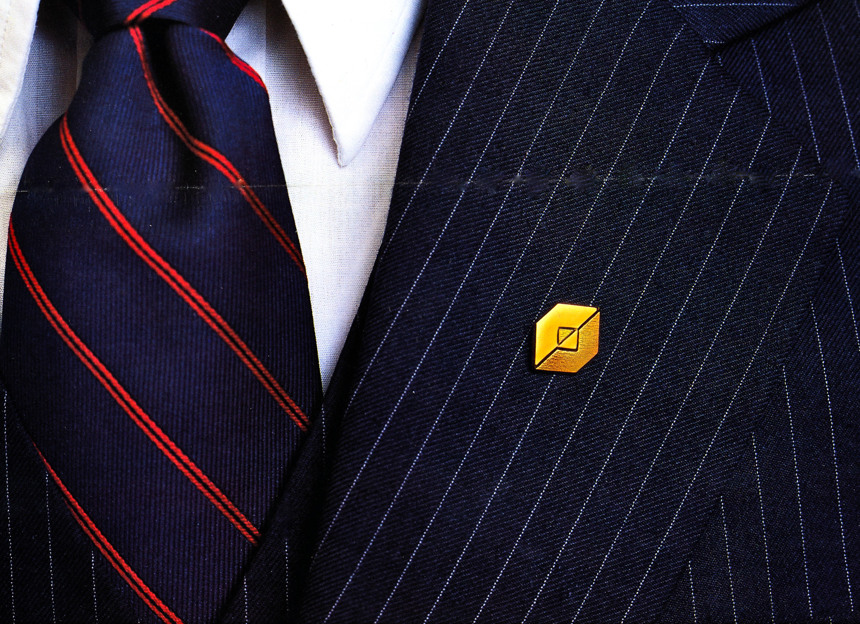 The new Fidelity logo as a gold pot metal lapel pin attached to the lapel of a suit.