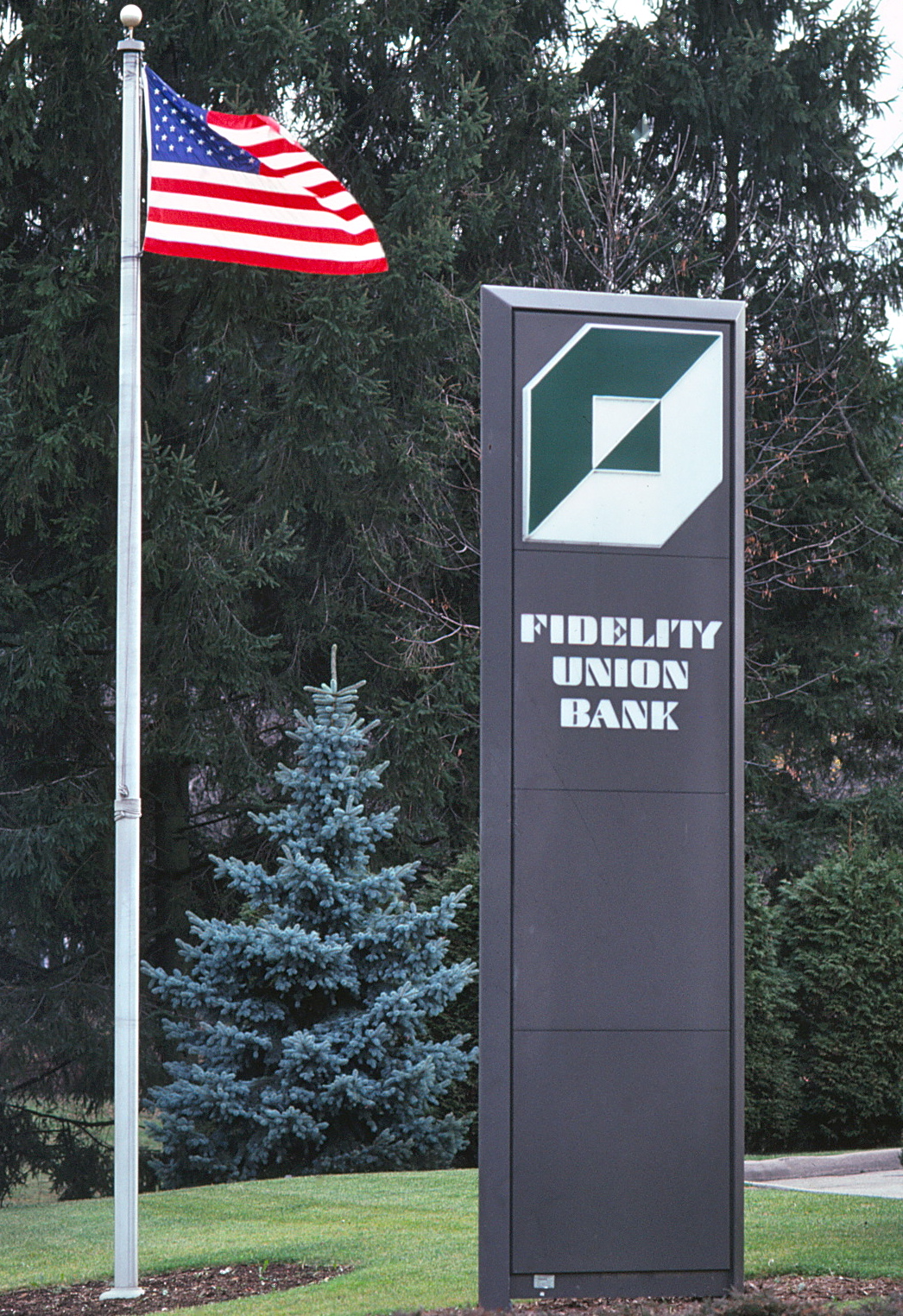 Outdoor photo of a tall pylon with Fidelity logo and typeface next to a fluttering US flag.